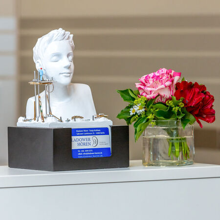 Büste mit Hörgeräten und Blumenstrauß auf Tresen in einem Hörakustik-Fachgeschäft.